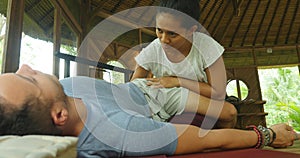 Young beautiful and exotic Asian Indonesian therapist woman giving traditional Thai massage to man relaxed at tropical wellness