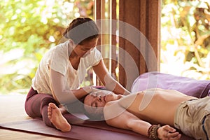 Young beautiful and exotic Asian Thai therapist woman giving traditional head and facial Balinese massage to Caucasian man in