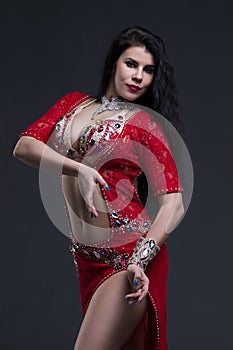 Young beautiful exotic eastern women performs belly dance in ethnic red dress on gray background