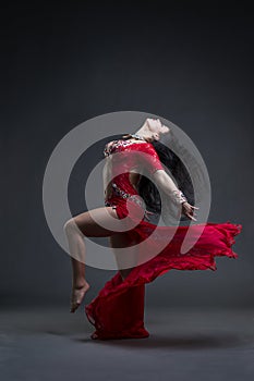 Young beautiful exotic eastern women performs belly dance in ethnic red dress on gray background