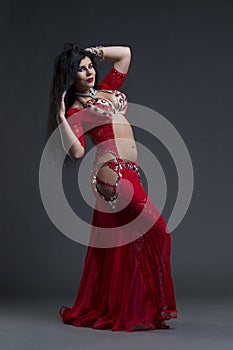 Young beautiful exotic eastern women performs belly dance in ethnic red dress on gray background