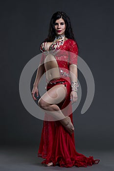 Young beautiful exotic eastern women performs belly dance in ethnic red dress on gray background