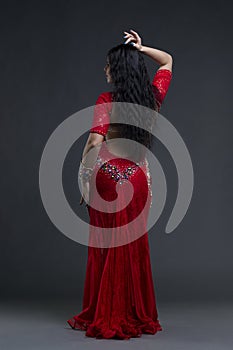 Young beautiful exotic eastern women performs belly dance in ethnic red dress on gray background