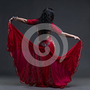 Young beautiful exotic eastern women performs belly dance in ethnic red dress with open back on gray background