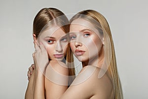 Young beautiful faces of two adult girls with bare shoulders on grey background