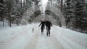 Young beautiful family having fun with a dog in winter forest. Man and woman running with beagle in forest.