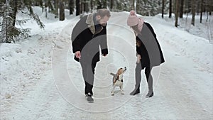 Young beautiful family having fun with a dog in winter forest. Man and woman walking with beagle in forest.