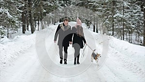 Young beautiful family having fun with a dog in winter forest. Man and woman walking with beagle in forest.