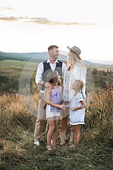 Young beautiful family posing and looking each other, while standing in a field, at summer sunset. Family relaxing in