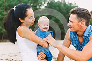 A young, beautiful family of three. Mom, Dad and daughter in the arms of my father play, rejoice, smile on the sandy beach on the