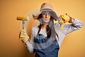 Young beautiful farmer woman wearing apron and hat holding fork with cob corn with angry face, negative sign showing dislike with