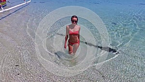 Young and beautiful fashion female model in red bikini lying on the waves in the sea. Fashion shooting. Aerial video in