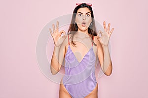 Young beautiful fashion girl wearing swimwear swimsuit and sunglasses over pink background looking surprised and shocked doing ok