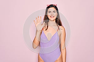 Young beautiful fashion girl wearing swimwear swimsuit and sunglasses over pink background showing and pointing up with fingers