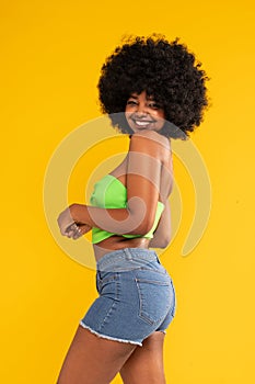 Young beautiful and fashionable cherful woman with afro hair, wearing casual clothes, posing over yellow studio background photo