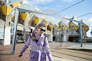 Young beautiful fashionable girl on a background of Yellow Cube houses in Rotterdam under Clear Blue Sky in Sunny Daytime,