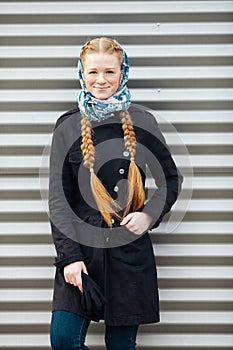 Young beautiful fashionable redhead woman with braids hairdo in blue white headcraft stylish denim black trench jacket posing outd