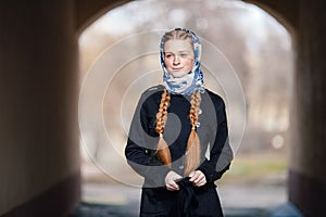 Young beautiful fashionable redhead woman with braids hairdo in blue white headcraft stylish denim black trench jacket posing outd