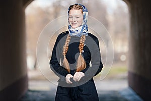 Young beautiful fashionable redhead woman with braids hairdo in blue white headcraft stylish denim black trench jacket posing outd