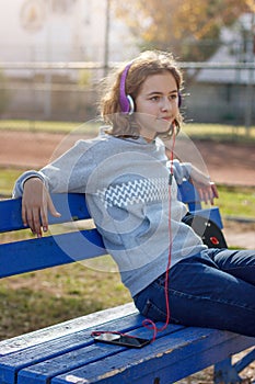 Young beautiful fashionable teenager girl listens to music on headphones from a smartphone