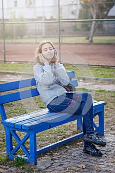 Young beautiful fashionable teenager girl listens to music on headphones from a smartphone