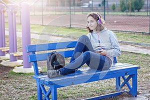 Young beautiful fashionable teenager girl listens to music on headphones from a smartphone