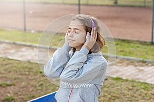 Young beautiful fashionable teenager girl listens to music on headphones from a smartphone