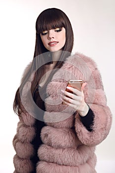 Young beautiful fashionable woman in pink fur coat holding mobil