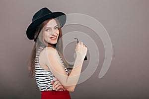 Young beautiful fashionable woman with trendy makeup in black hat and glasses on the grey background . Model looking at camera, w