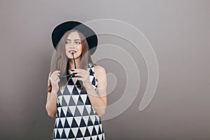 Young beautiful fashionable woman with trendy makeup in black hat and glasses on the grey background . Model looking at camera, w