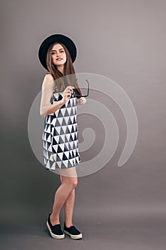 Young beautiful fashionable woman with trendy makeup in black hat and glasses on the grey background . Model looking at camera, w
