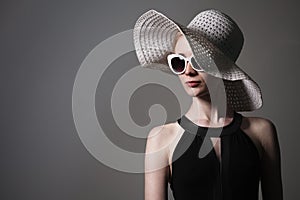 Young beautiful fashionable woman with trendy makeup. Model looking at camera, wearing stylish eyeglasses, hat. Female