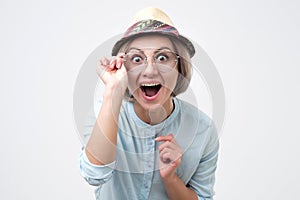 Young beautiful woman wearing pretty summer hat and sunglasses is opening mouth in surprise