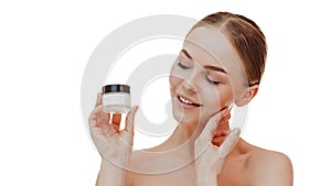 Young beautiful female with closed eyes applying face cream to cheekbones as part of morning routine, isolated on white background