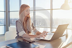 Young beautiful female copywriter typing texts and blogs in spacious light office, her workplace, using pc keyboard