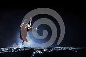 Young and beautiful female dancer in a red dress jumping