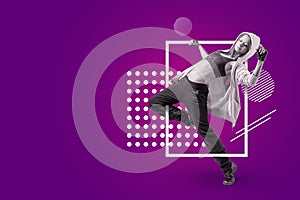 A young beautiful female dancer in sleeveless crop top, sweatpants and hoodie dancing on a purple background with white