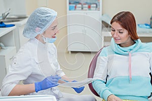 Young beautiful female dentist is talking to her patient. Red-haired woman smiling at the reception at the doctor
