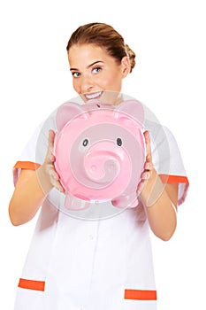 Young beautiful female doctor or nurse holding a piggybank