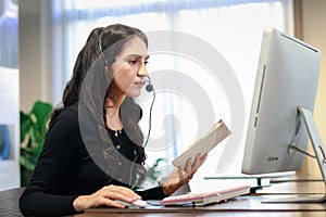 Young beautiful female with headphones working at call center service desk consultant, talking with the customer on hands-free
