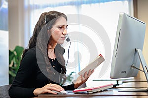 Young beautiful female with headphones working at call center service desk consultant, talking with the customer on hands-free