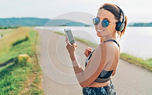 Young beautiful female listening to music using smartphone and  wireless headphones and starting jogging and cheerfully smiling in