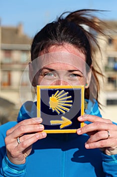 Young beautiful female pilgrim`s portrait posing with the typical `Camino de Santiago` blue tile painted with a yellow shell