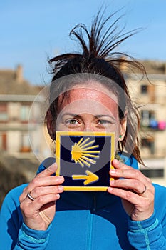 Young beautiful female pilgrim`s portrait posing with the typical `Camino de Santiago` blue tile painted with a yellow shell