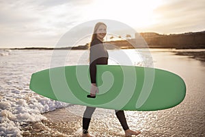 Young Beautiful Female Surfer With Surfboard Posing On Beach At Sunset