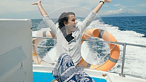 Young beautiful female traveler in casual clothing is having cruise on board of a yacht at the open sea. Happy woman is