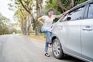 Young beautiful female using force trying to unscrew the wheel bolts nuts with the car jacked up changing wheel