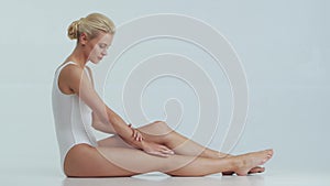Young, beautiful, fit and natural blond woman in white swimsuit applying skincare cream. Massage, skin care, cellulite
