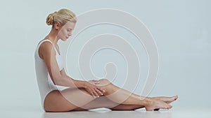 Young, beautiful, fit and natural blond woman in white swimsuit applying skincare cream. Massage, skin care, cellulite