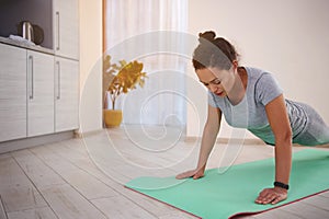 Young beautiful fit woman exercising pushups on a fitness mat at home on a sunny day. Home workout concept